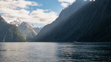 Güneşli bir günde fiyorttan geçen bir tekne. Fotoğraf Milford Sound, Fiordland Ulusal Parkı, Yeni Zelanda