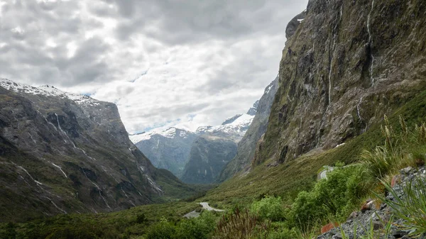 Vallée verte pleine de cascades et de montagnes enneigées en toile de fond prise de vue par temps couvert. Photo prise dans le parc national de Fiordland, Nouvelle-Zélande — Photo