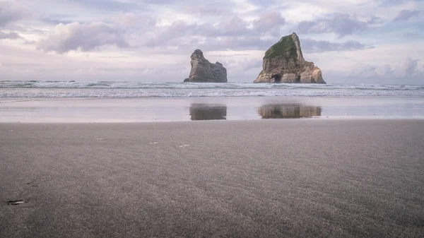 Escenario de playa al atardecer con dos islas remotas y cielo colorido en el telón de fondo. Disparo en Wharariki Beach, Nueva Zelanda — Foto de Stock