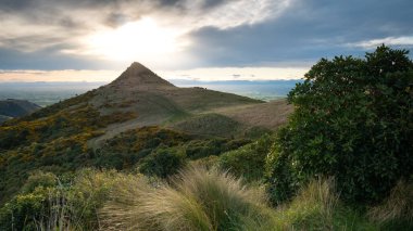 Güneş alışılmadık şekilli bir dağın ardında batıyor. Yeni Zelanda 'daki Christchurch civarındaki Port Hills bölgesinde gün batımı çekiliyor.