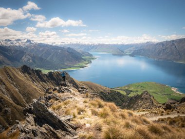 Kayanın kenarında duran adam yemyeşil çayırlar, mavi göl ve karlı dağlar ile güzel manzaranın tadını çıkarıyor. Isthmus Tepesi zirvesinde güneşli bir gün.