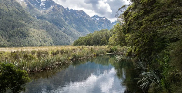 Vista pequena do lago emoldurada por árvores à direita e montanhas à esquerda. Foto tirada no Mirror Lakes em Fiordland National Park, Nova Zelândia — Fotografia de Stock
