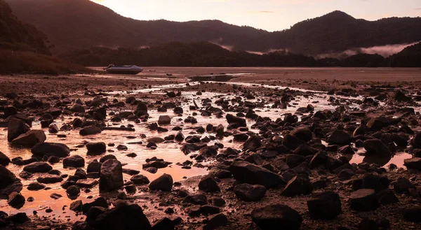 Tropikal körfezde kıpkırmızı bir gün batımı. Çerçevesinde terk edilmiş bir tekne. Abel Tasman Ulusal Parkı, Yeni Zelanda 'da peyzaj çekimi