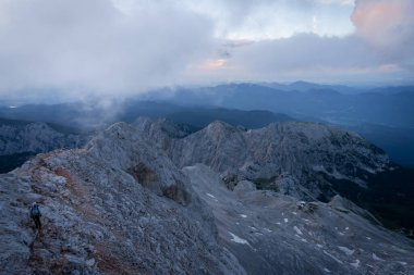 Slovenya 'nın renkli gündoğumu sırasında kayalık tepelerde yürüyüş yapan yürüyüşçünün geniş açılı görüntüsü.
