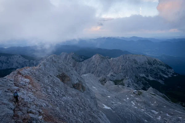 Slovenya 'nın renkli gündoğumu sırasında kayalık tepelerde yürüyüş yapan yürüyüşçünün geniş açılı görüntüsü.
