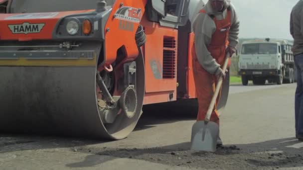 道路滚轮驱动和一名工人使用铲子 — 图库视频影像