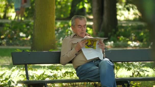 Älterer Mann Liest Zeitung Auf Einer Bank — Stockvideo