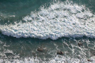 Denizde, köpüklü bir dalga kıyıya doğru yuvarlanıyor.