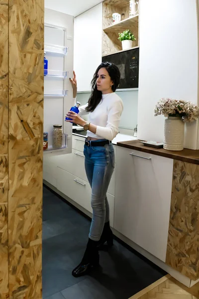 Young woman in front of the fridge gettiing a bottle of water