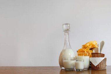 Süt şişesi ve bardakları, sarı çiçekleri ve sepetleri olan yatay beyaz telif alanı