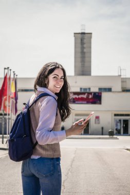 Öğrenci kızın dikey portresi geriye bakıp gülümsüyor.