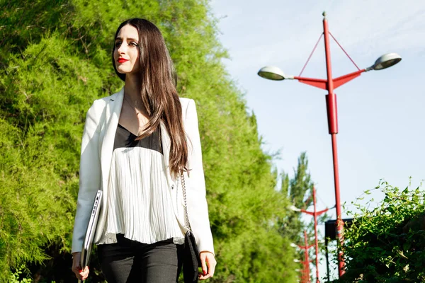 Yeşil bir sokakta yürüyen beyaz bir iş kadınının portresi.