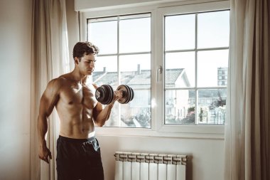 Formda genç bir adam evde dambılla çalışıyor.