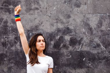 Tarafsız arka planda gökkuşağı kolluklu genç lezbiyen yumruk kaldırıyor. Uzayı kopyala LGBT gücü.