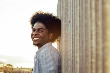 Sokakta duvara yaslanmış gülümseyen yakışıklı siyah afro adamın portresi.