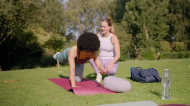 İki kadın parkta eğitmenle yoga yapıyor.