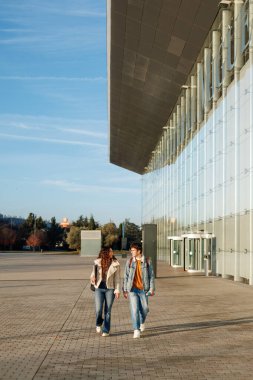 Modern üniversite kampüsünde çeşitli öğrenciler yürüyüp konuşuyor.
