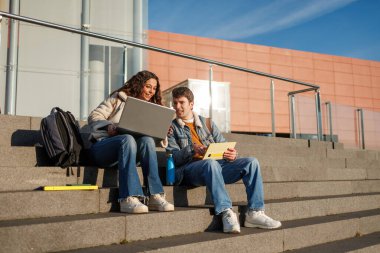Üniversite öğrencileri kampüs basamaklarında çalışıyor.