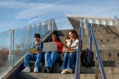 Kampüs basamaklarında oturan çeşitli öğrenciler birlikte öğreniyorlar.