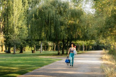 Parkta yoga minderiyle yürüyen Afrikalı Amerikalı kadın.