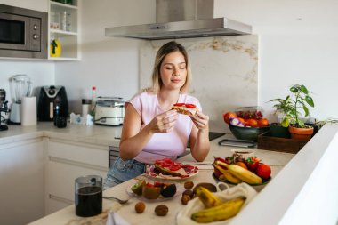Kadın kahvaltıda sağlıklı bir tostun ve taze meyvenin tadını çıkarıyor.
