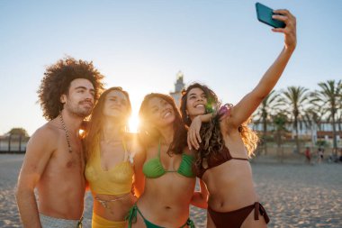 Mutlu arkadaşlar gün batımında sahilde selfie çekiyorlar.