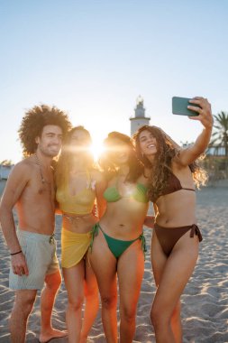 Arkadaşlar sahilde yaz günbatımının keyfini çıkarıyorlar.