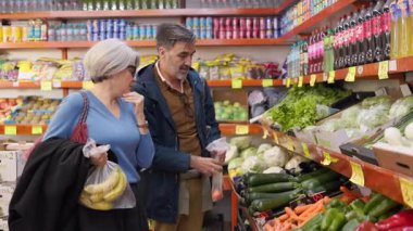 Olgun çift süpermarket koridorunda taze ürün alışverişi yapıyor.