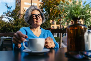Sunny Outdoor Terasında kahvenin tadını çıkaran son sınıf kadını.