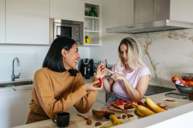 Modern bir mutfakta eğlenceli bir kahvaltı deneyimini paylaşan mutlu kadınlar.