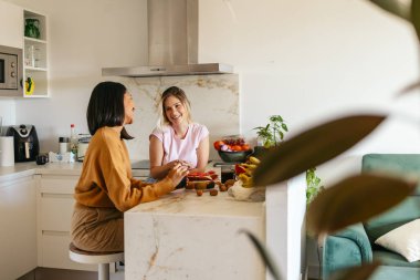 Mutlu lezbiyen çift sabah yemeğinin tadını çıkarıyor ve parlak evlerinin mutfağında sohbet ediyorlar.