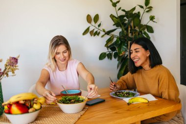 Mutlu kadın arkadaşlar öğle yemeğinde sağlıklı salata yerler, evde yemek yerler.