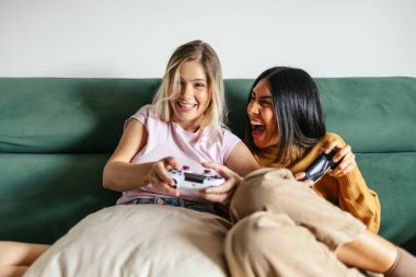 Evdeki kanepede video oyunu oynayan mutlu kadınlar.