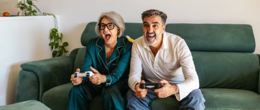 Mutlu son sınıf çifti evde video oyunlarını seyrediyor, yeşil bir kanepede oturuyor.