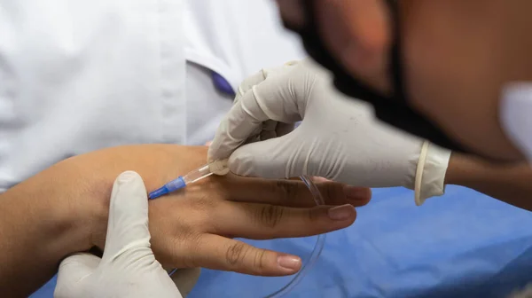 hands with doctors glove insert needle into patients hand