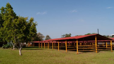 Ağıllar ya da boş sığır ahırları, arka planda ağaçlar ve yukarıda gökyüzü.