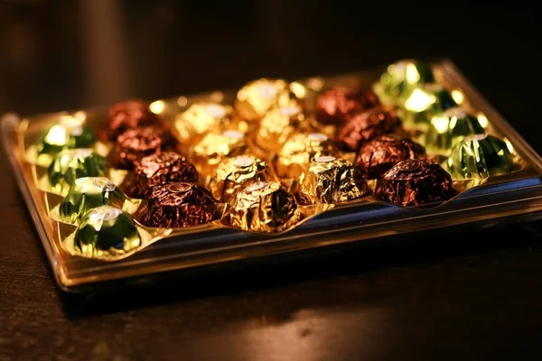 Altın ambalajlı çikolatalı pralinler, karanlık oda, tahta masa.