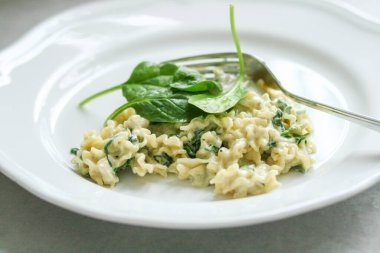 Mascarpone peyniri soslu Mafalde Makarnası ve gümüş çatallı beyaz tabakta ıspanak.