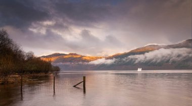 The Hills over Loch Lomond in Scotland lit by early morning sun and surrounded by low cloud clipart