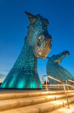 Falkirk, Scotland- April 24th 2021; The Kelpies in Falkirk lit up in blue at dusk. The colours will change throughout the night time hours. clipart