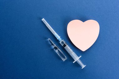 Aşısı olan tıbbi ampuller ve mavi arka planda kalp şeklinde bir çıkartma..