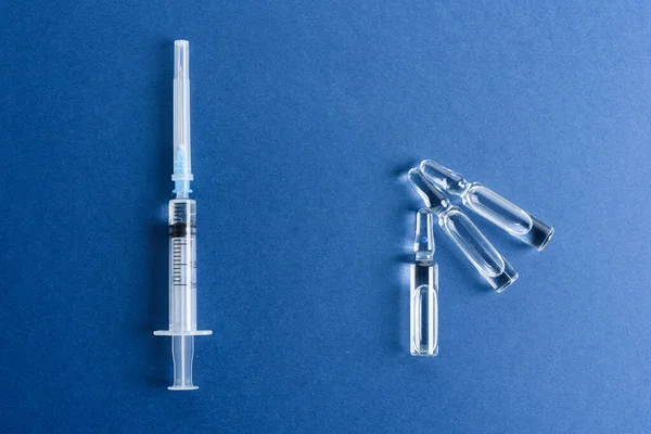 Ampolas com vacina e seringa sobre fundo azul. — Fotografia de Stock