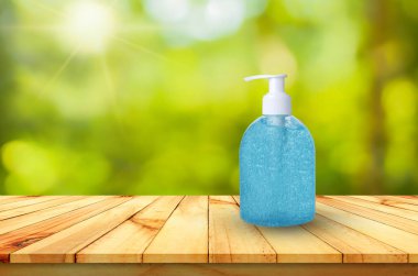 Alkol ellerini yıkar, jel ahşap bir masanın üzerinde doğal yeşil bokeh arkaplanıyla..