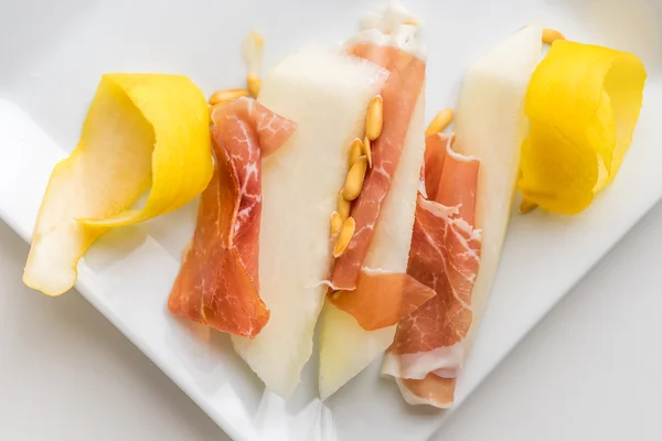 Platte weergave van prosciutto segmenten met gele citroen. Zaden en schil. Voedsel op witte plaat. — Stockfoto