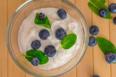 Yoğurt ve nane ile yaban mersini yapraklar üzerinde ahşap masa. Yaban mersini ile yoğurt ve nane şeffaf kase. Şeffaf kase yoğurt, yaban mersini ve nane ile. Yumuşak odak. Üst veya düz görünüm.