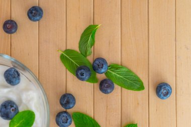 Yoğurt ve nane ile yaban mersini yapraklar üzerinde ahşap masa. Yaban mersini ile yoğurt ve nane şeffaf kase. Şeffaf kase yoğurt, yaban mersini ve nane ile. Yumuşak odak. Üst veya düz görünüm.