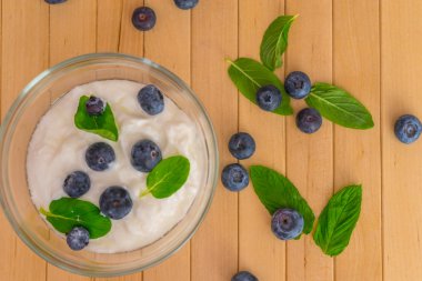 Yoğurt ve nane ile yaban mersini yapraklar üzerinde ahşap masa. Yaban mersini ile yoğurt ve nane şeffaf kase. Şeffaf kase yoğurt, yaban mersini ve nane ile. Yumuşak odak. Üst veya düz görünüm.