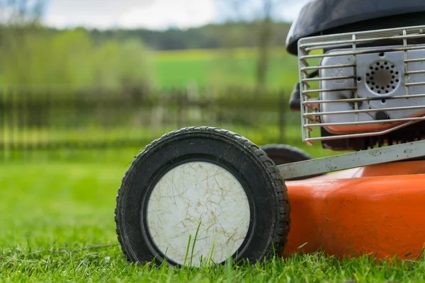 Tekerlek ve çim biçme makinesi (çim kesici) motorlu Ahşap korkuluk, çim sahası, ağaçlar ve gökyüzü arka plan üzerinde düzenlenen çimenlerin üzerinde bir ayrıntı. Yumuşak odak / sığ derinlik