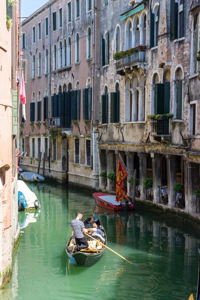 VENECIA, ITALIA - 23 de mayo de 2016: Gondolier con pasajeros en góndola viajando a través de la hermosa y colorida Venecia. Venecia edificios y canal con gondolero durante el día brillante . — Foto de Stock