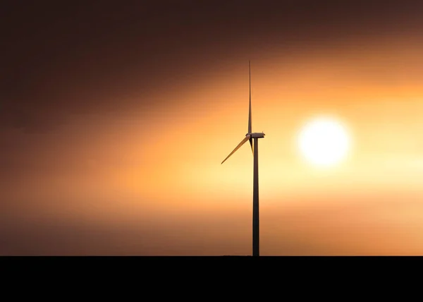 一个用来发电的高电动风车在橙色日落时的轮廓中 透过浓烟和云彩 太阳是可见的 这是一个极简主义的场景 — 图库照片